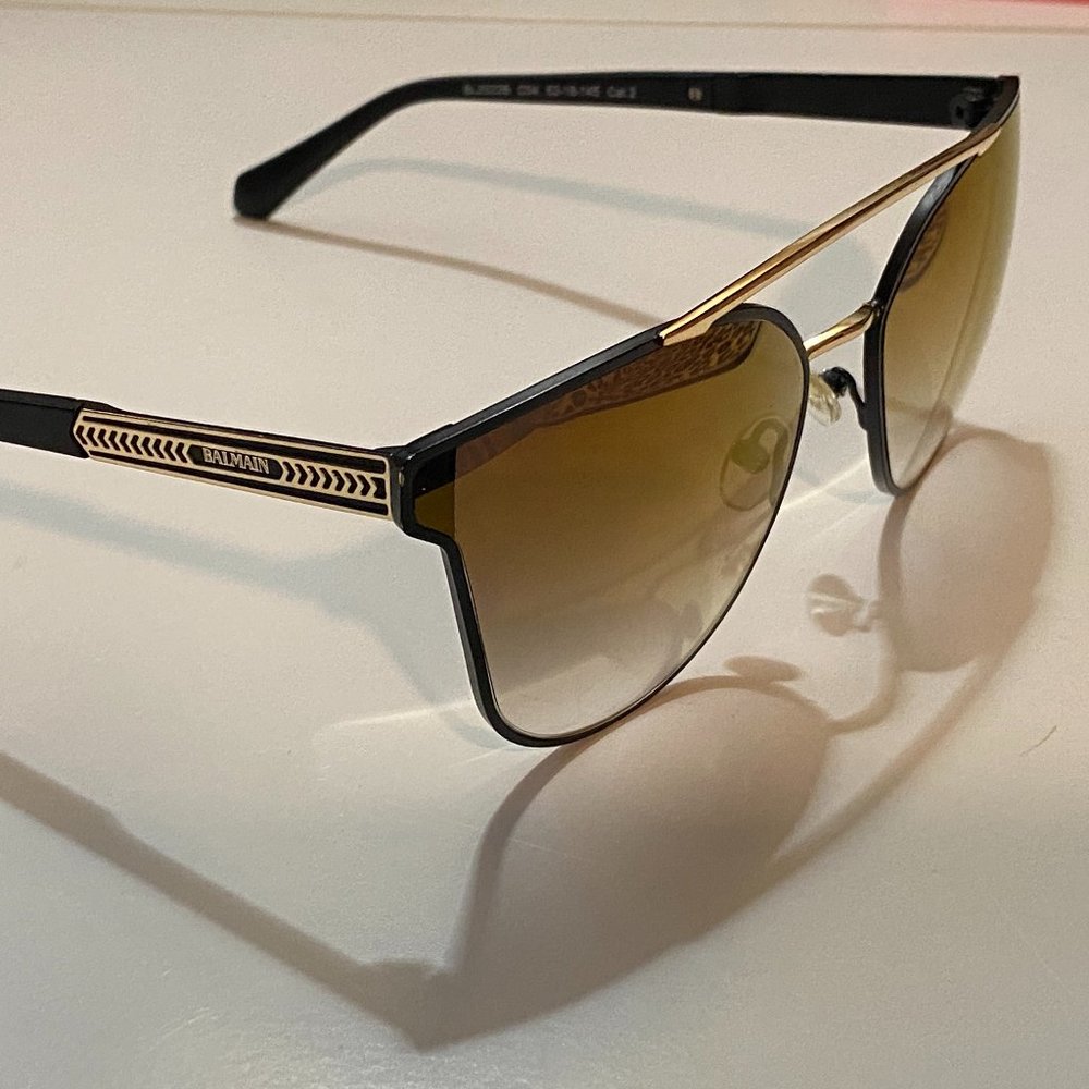 Balmain; matte black + bright gold accent; mirrored gold ombre lens